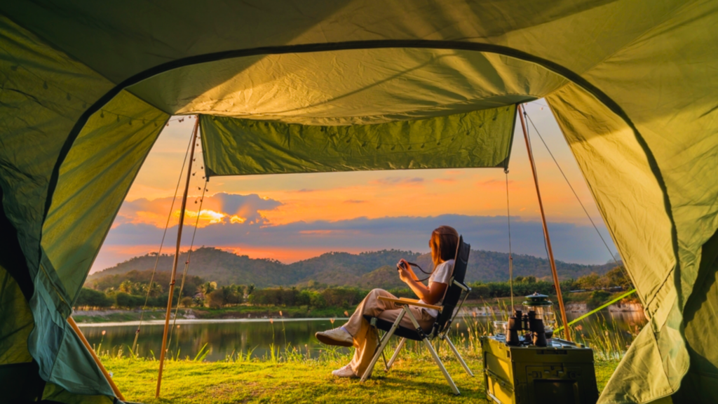 Woman enjoying coffee outside of her tent while camping looking at the sunrise