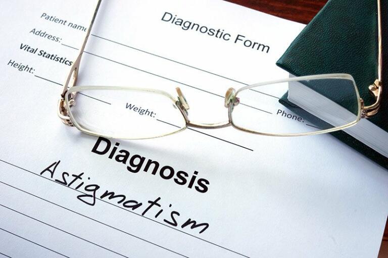 diagnosis form with astigmatism written on it, glasses resting on top