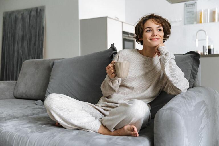 woman sitting crosslegged on gray couch with mug in her hand after SMILE eye surgery