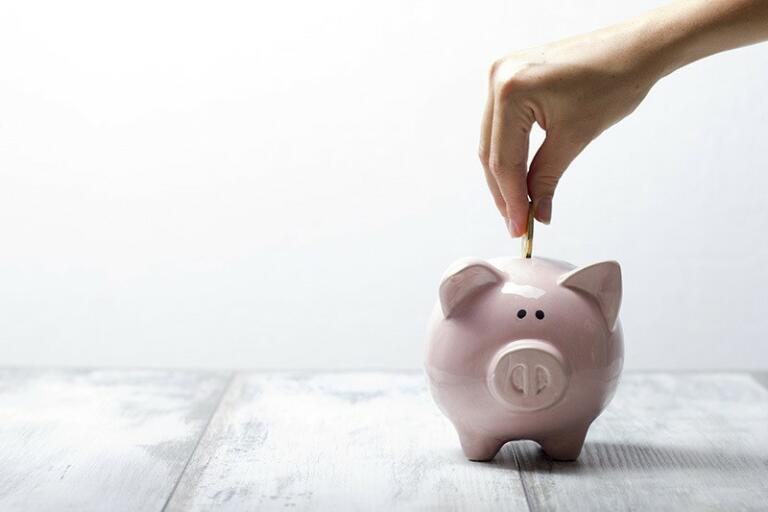 hand putting gold coin into a pink piggy bank with a white background