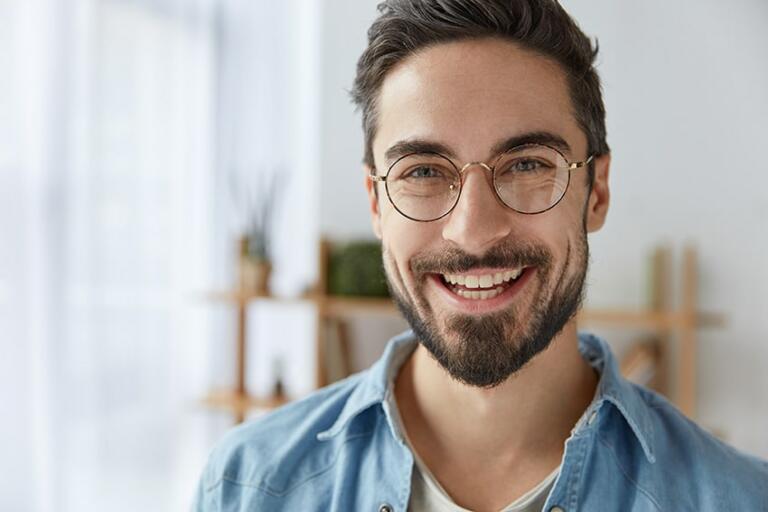 Close up shot of a man with a big smile, wearing round spectacles