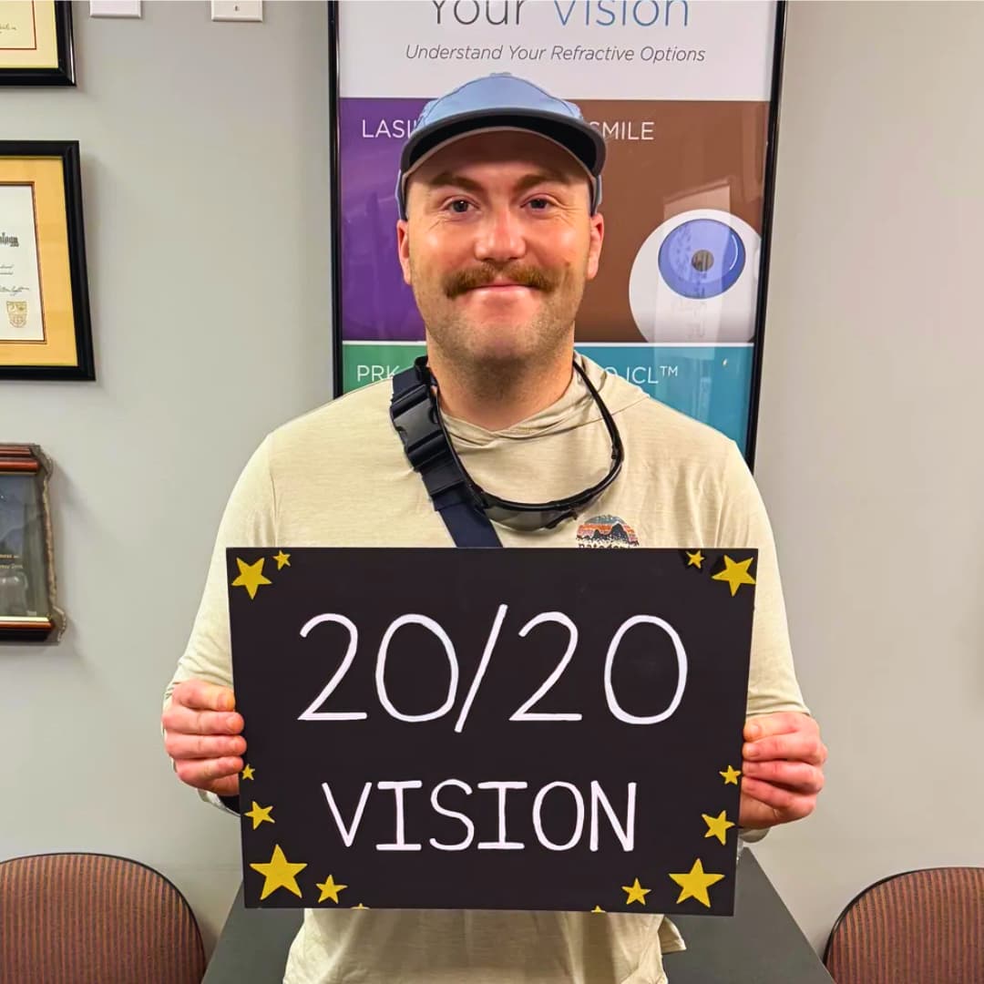 Happy post-op PRK (photorefractive keratotomy) patient at LaserVue Eye Center smiles for the camera while holding a sign that reads "20/20 Vision"