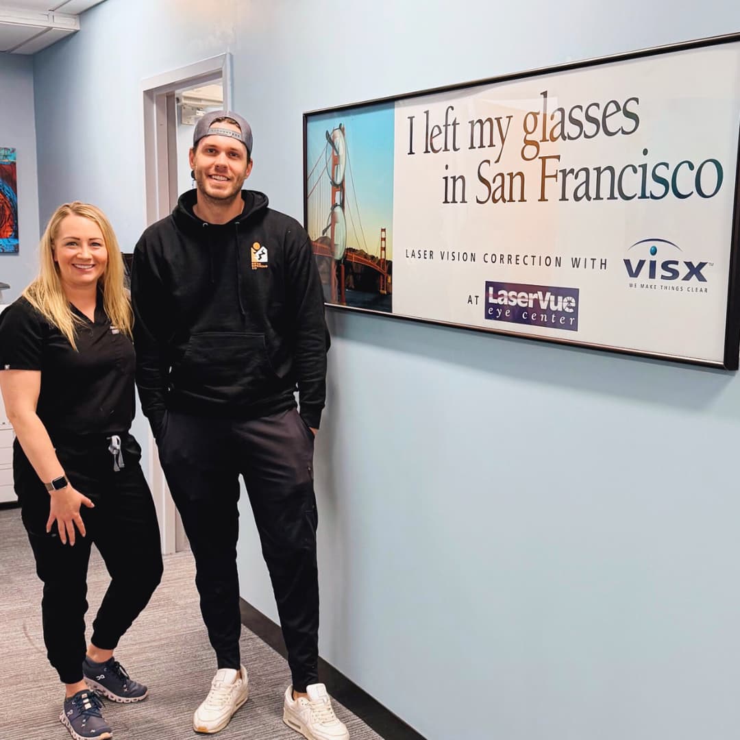 Happy LASIK patient stands with Dr. Hannah Walsh next to a sign that reads "I left my glasses in San Francisco. Laser Vision Correction with LaserVue Eye Center"
