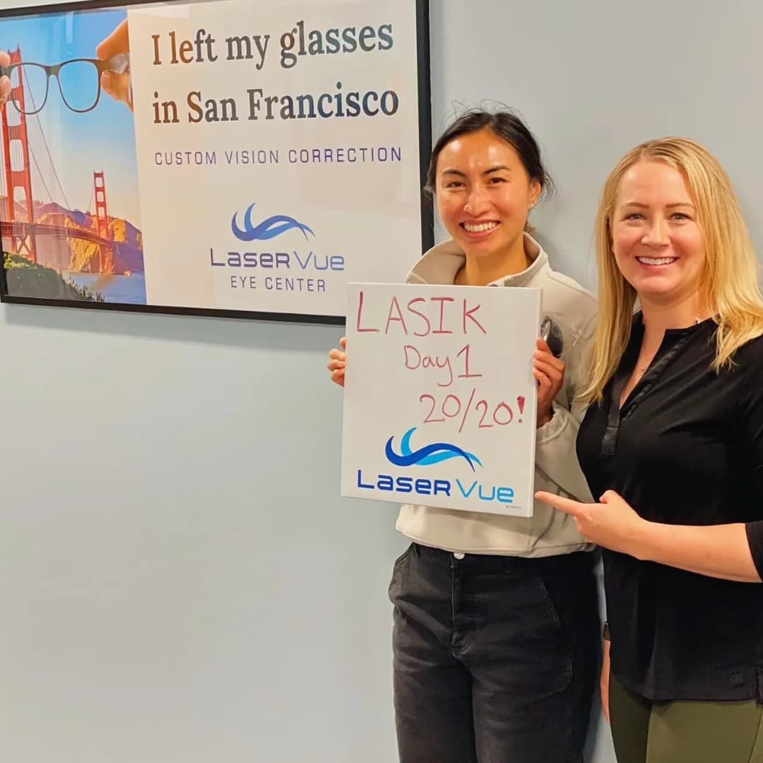 Happy woman who just got LASIK at LaserVue stands with Dr. Hannah Walsh holding a sign that reads "LASIK Day 1 20/20! LaserVue", standing behind a sign that reads "I left my glasses in San Francisco. Custom Vision Correction with LaserVue Eye Center"