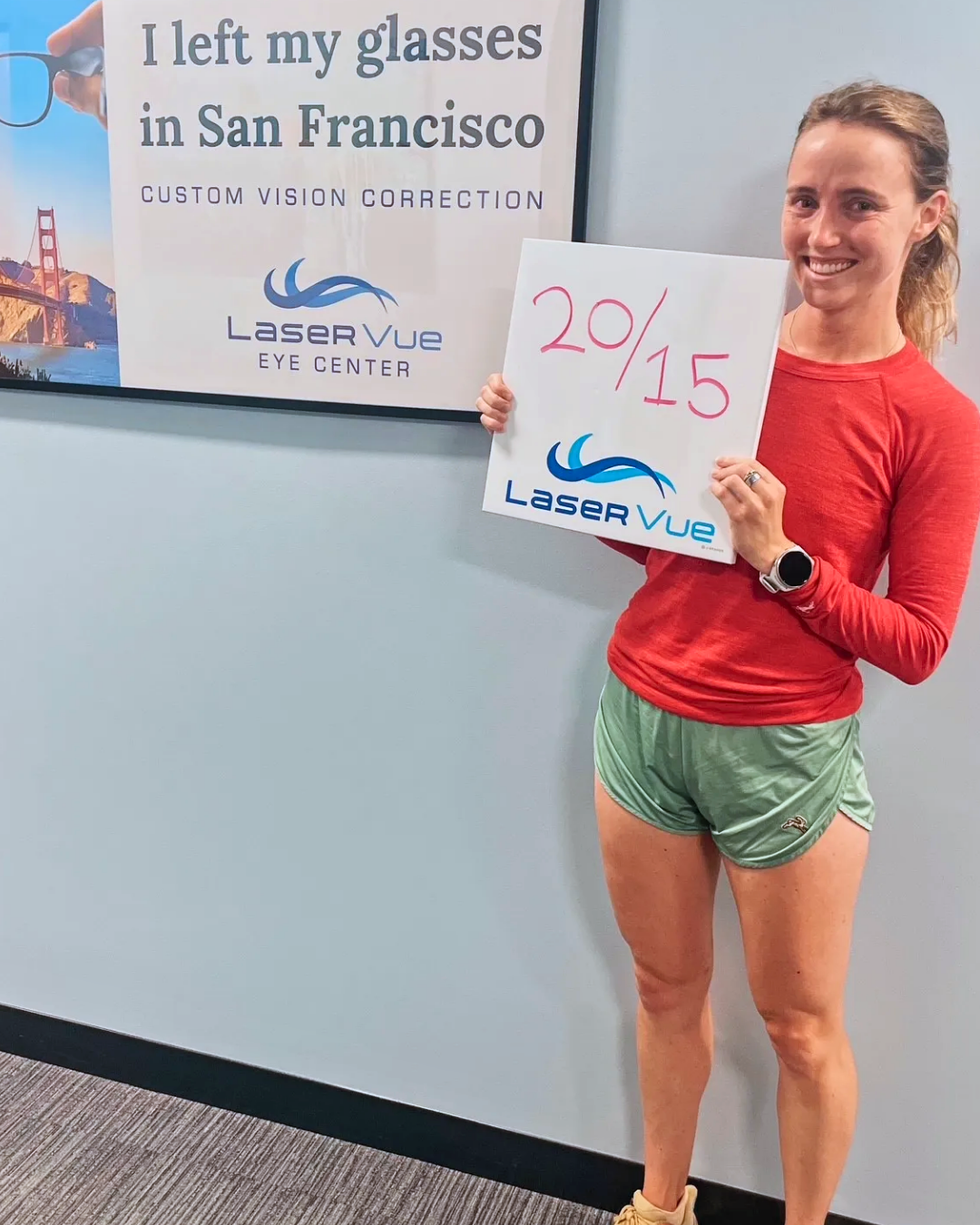 LaserVue LASIK Patient, Meredith R., stands holding a whiteboard that reads "20/15. LaserVue." while standing in front of a poster that reads "I left my glasses in San Francisco. Custom vision correction with LaserVue Eye Center."