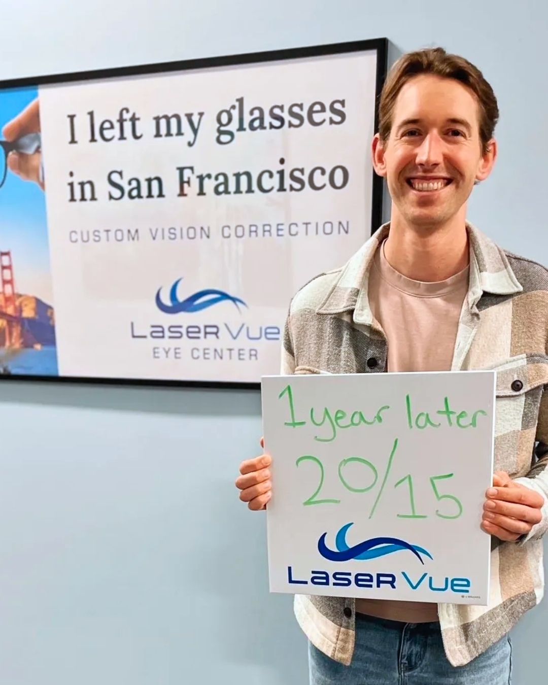 Happy LASIK patient attends his 1-year post-op exam at LaserVue Eye Center. He smiles while holding a whiteboard that reads "1 year later. 20/15. LaserVue." Behind him is a poster that reads "I left my glasses in San Francisco. Custom vision correction with LaserVue Eye Center."