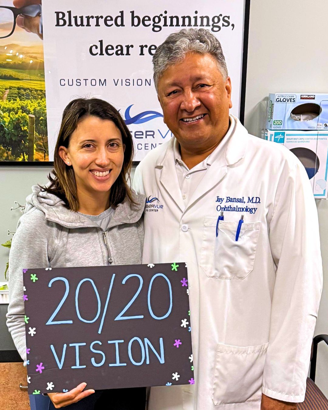 Happy LASIK patient stands next to Dr. Jay Bansal, ophthalmologist and LASIK surgeon at LaserVue Eye Center Santa Rosa. The patient is holding a sign that reads "20/20 Vision". The patient and Doctor are standing in front of a poster that reads "Blurry beginnings, clear results. Custom vision correction with LaserVue Eye Center."