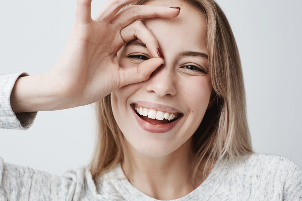 Smiling woman holding an OK gesture over one eye