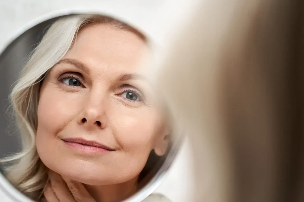 Woman in her 50s and above smiles while using a magnified vanity mirror to check her complexion
