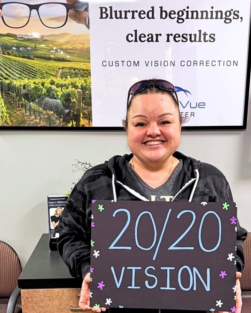 LASIK patient at LaserVue Eye Center celebrates their 20/20 vision. They are standing, holding a sign that reads "20/20 vision".