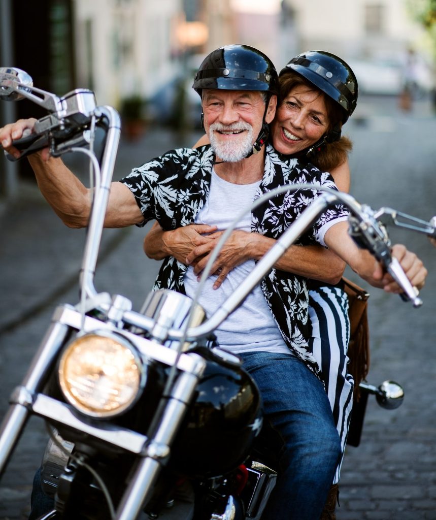 cheerful senior couple travellers with motorbike in town.