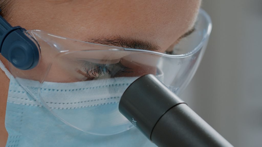 Laboratory technician in mask and goggles using a microscope