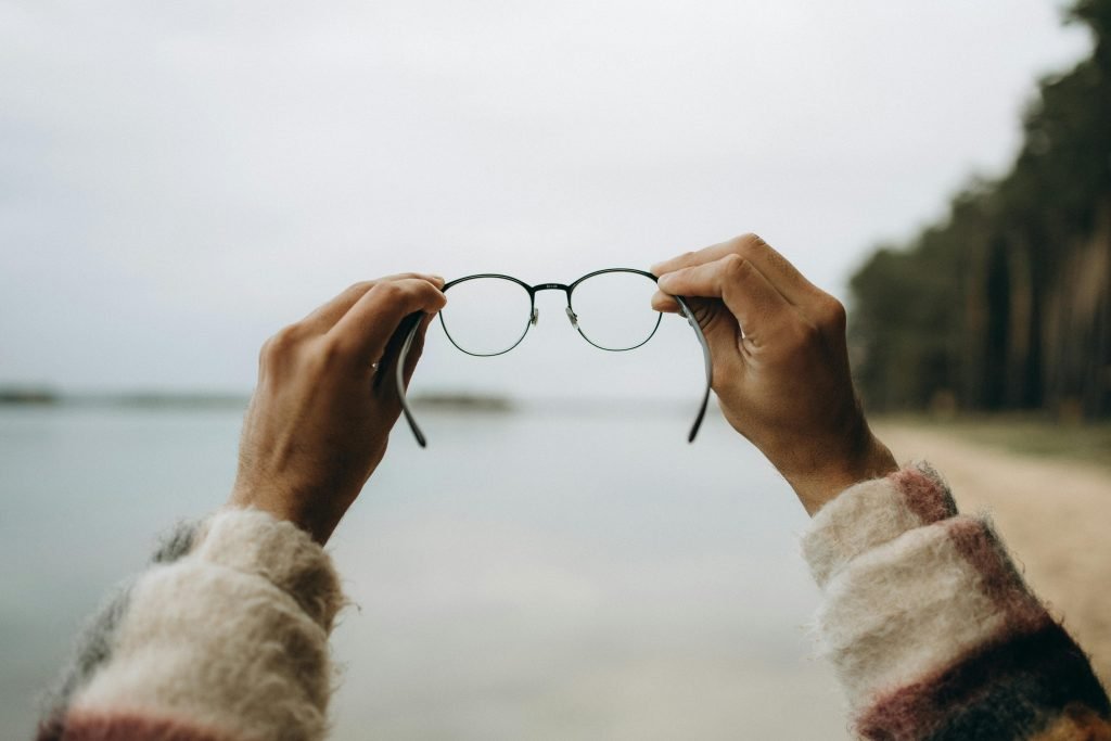Hands holding eyeglasses with a blurred sea background