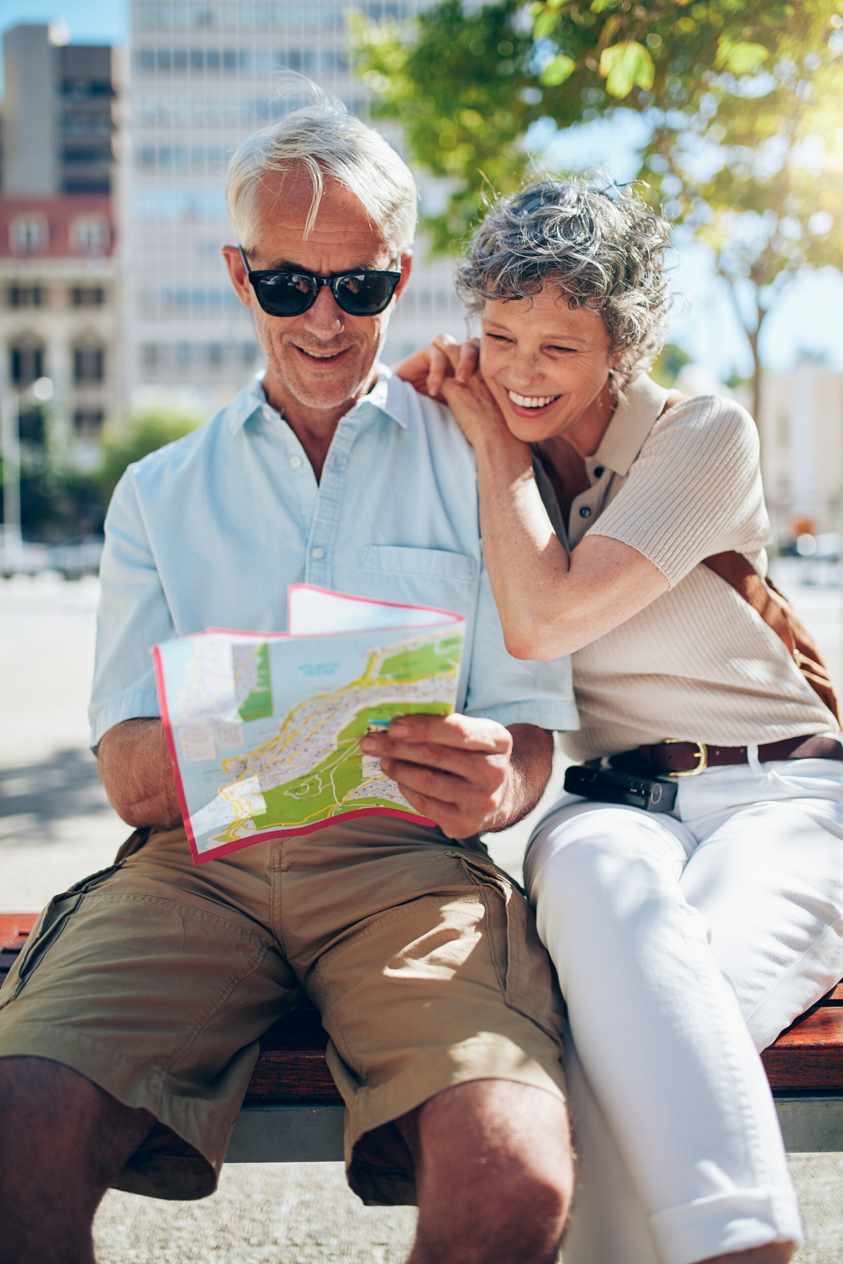 Senior couple sitting together on a bench in the city looking at city map for directions. Mature man and women tourist using city map.