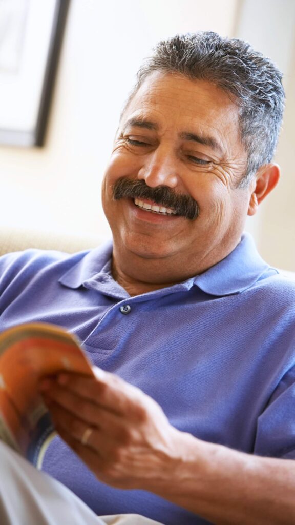 Older Hispanic man with mustache is happily reading a book with clear vision.