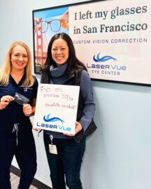 Dr. Nicole Luu, PharmD, BCPS, stands with Dr. Hannah Walsh, optometrist at LaserVue Eye Center. Dr. Luu is holding a whiteboard that reads "Prescribed EVO ICL, 20/20, no refills needed! LaserVue." Dr. Luu and Dr. Walsh are standing in front of a poster that reads "I left my glasses in San Francisco. Custom Vision Correction. LaserVue Eye Center."