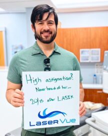 Happy LaserVue patient after his LASIK procedure, Jeremy F., stands and smiles holding a sign that reads "High astigmatism? Never heard of her... 20/15 after LASIK. LaserVue."