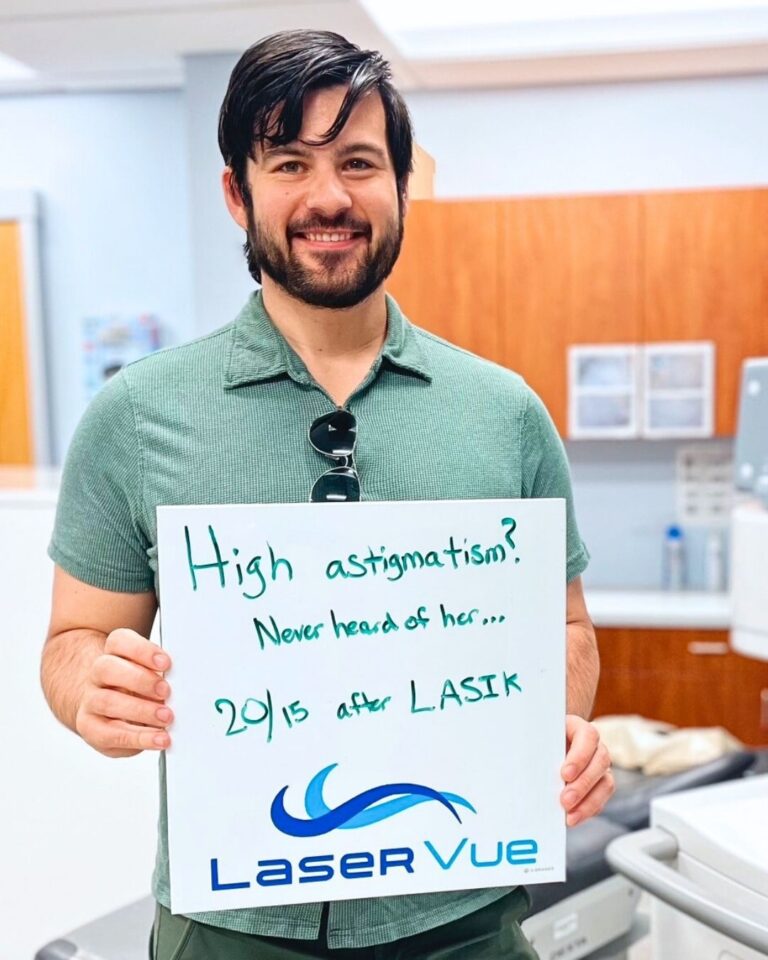 Happy LaserVue patient after his LASIK procedure, Jeremy F., stands and smiles holding a sign that reads "High astigmatism? Never heard of her... 20/15 after LASIK. LaserVue."