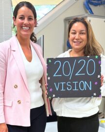 Happy LASIK patient Kaya E. stands at LaserVue Eye Center with Dr. Francesca Sefton, optometrist. The patient is holding a hand painted sign that reads "20/20 vision".