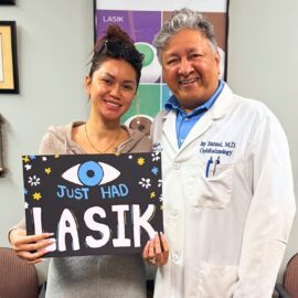 Happy LASIK patient stands next to Dr. Jay Bansal holding a sign that reads "(Eye) Just Had LASIK."