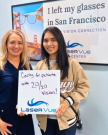 Happy woman stands with Dr. Hannah Walsh, optometrist at LaserVue Eye Center. Holding a whiteboard that reads "Caring for patients with 20/20 vision! LaserVue." She and Dr. Walsh are standing in front of a poster that reads "I left my glasses in San Francisco. Custom Vision Correction. LaserVue Eye Center."