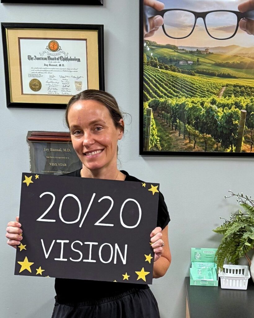 Molly M. LASIK 20/20 vision patient standing, holding a sign that reads "20/20 vision" at LaserVue Eye Center