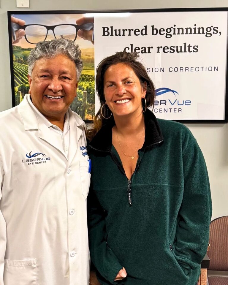 Happy SMILE patient, Taylor M, stands with Dr. Jay Bansal at LaserVue Eye Center. The patient and doctor stand in front of a poster that reads "Blurred beginnings, clear results. Custom vision correction with LaserVue Eye Center."