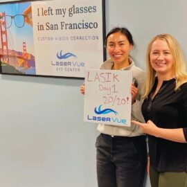 Happy woman who just got LASIK at LaserVue stands with Dr. Hannah Walsh holding a sign that reads "LASIK Day 1 20/20! LaserVue", standing behind a sign that reads "I left my glasses in San Francisco. Custom Vision Correction with LaserVue Eye Center"