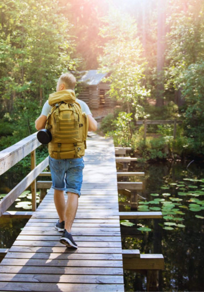 Man walks across a wooden bridge over a lily pond, while looking at the sunny sky.