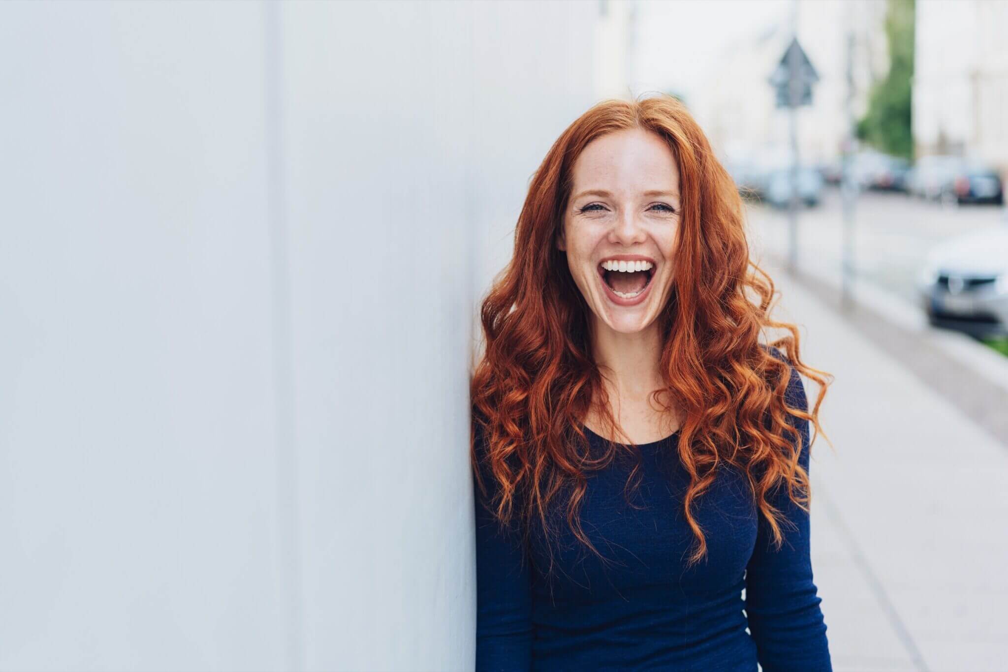 Woman with a lovely sense of humour standing leaning against a white exterior wal